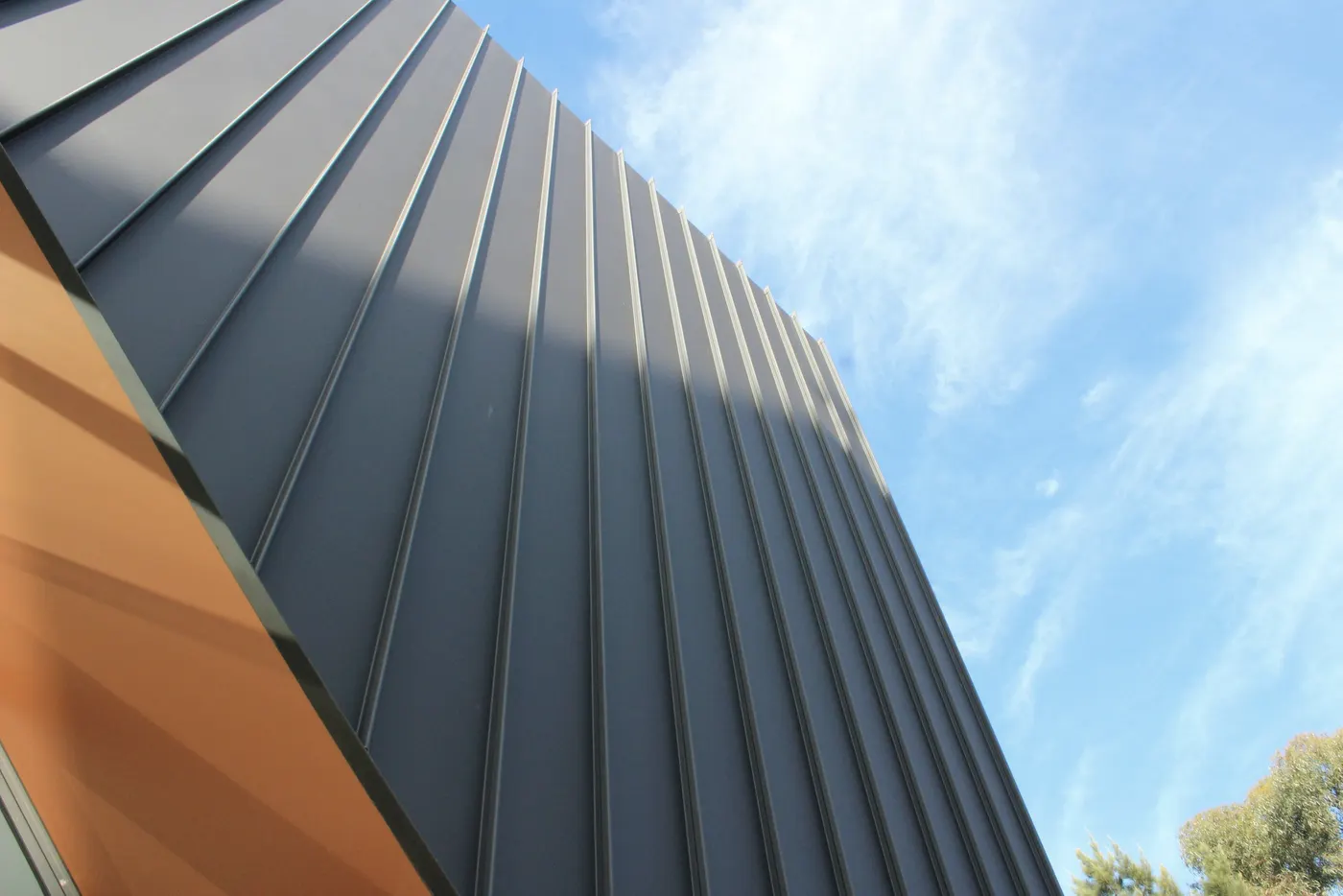 Close view of standing-seam metal panels in raking light beside a cedar-clad edge.