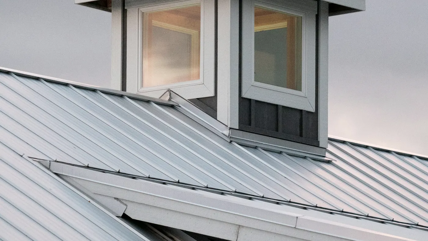 Silver standing-seam roof with a cupola, hips, and hemmed edges at dusk.